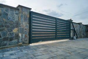 Wide automatic sliding gate with remote control installed in high stone fense wall. 