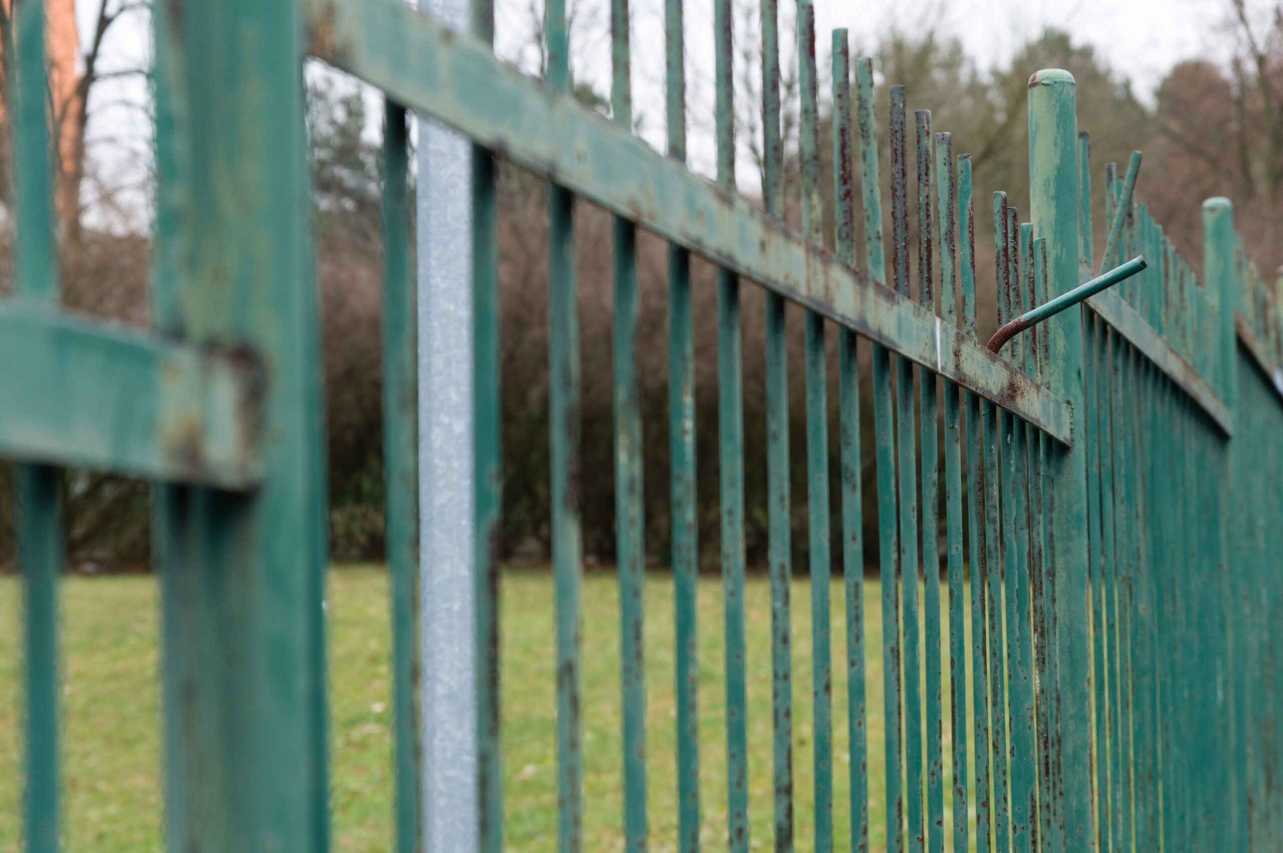 Rusty and weathered green painted metal fence by top rail fence