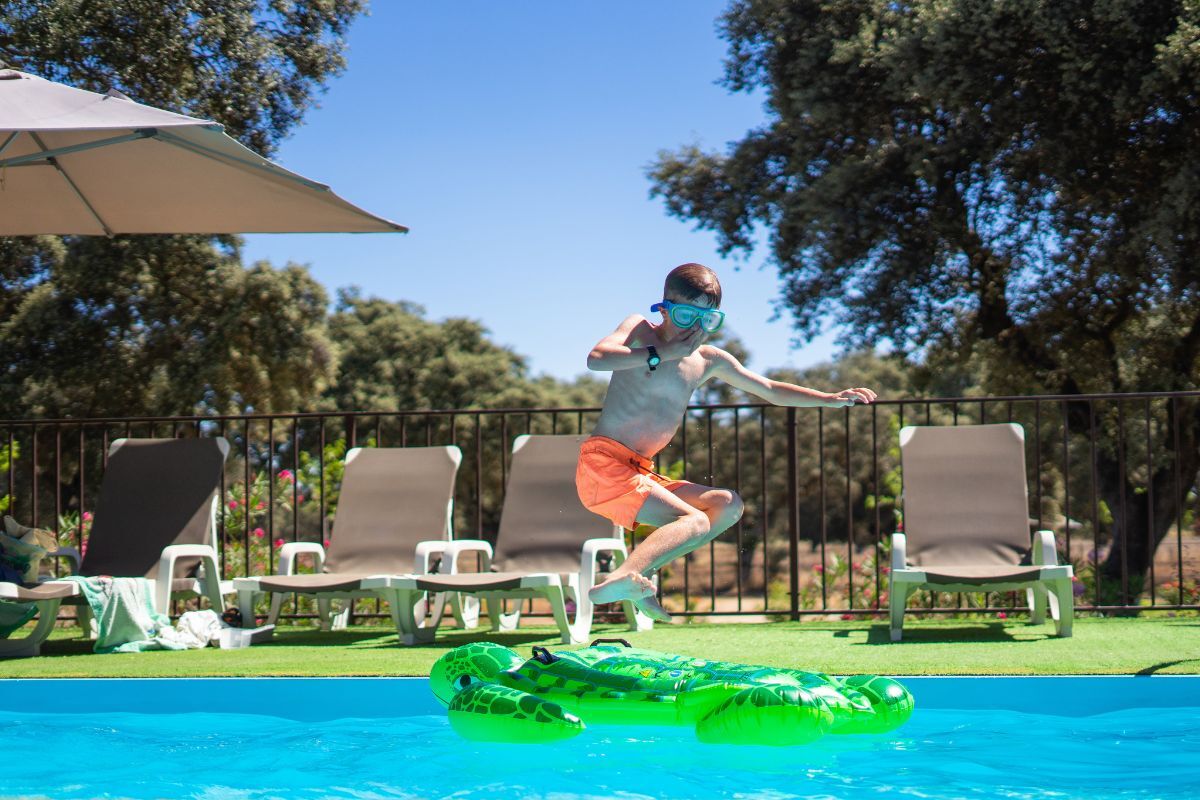 Young boy jumping into a pool with a ornamental fence in the background