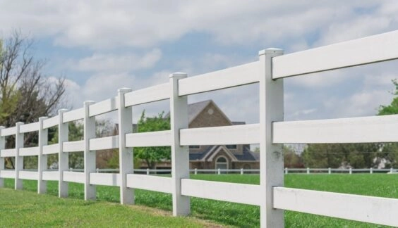 White vinyl farm fence near a home in countryside