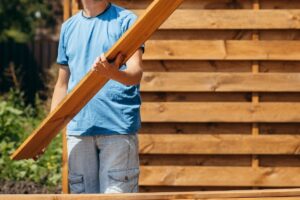 Man looking at a wooden fence panel while working on installing a horiztonal fence.